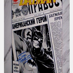 Peut inclure: Une bande dessinée Batman vintage avec une couverture de style journal russe. Le titre "Batman" est en jaune, et la couverture présente une illustration en noir et blanc de Batman. Le texte "American Hero" est visible.