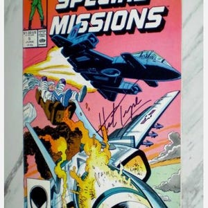 May include: GI JOE Special Missions comic book cover featuring a jet, explosions, and figures in flight. The cover has the Marvel logo and issue number 5. The comic is signed by the artist. The background is a mix of pink, orange, and blue.
