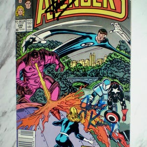 May include: A Marvel The Avengers comic book issue 299, dated January, featuring a colorful action scene with Mr. Fantastic, Invisible Woman, and Captain America battling a purple robot. The cover includes black ink signatures and the text.