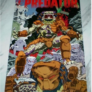 May include: A comic book cover featuring the word "PREDATOR" in red block letters. The image depicts a Predator character in orange and green armor, holding a weapon. Other Predator figures are in the background, with a cityscape and explosions.