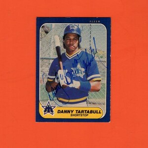 May include: A baseball card featuring Danny Tartabull, a short stop, in a blue uniform with a star logo. The card has a blue border and the Fleer logo. The image includes an autograph.