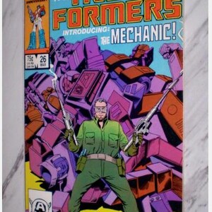 May include: A vintage comic book cover for The Transformers, featuring a green-clad character holding two silver tools, with a purple and orange robot in the background. The cover text reads "MORE THAN MEETS THE EYE" and "INTRODUCING: THE MECHANIC!"