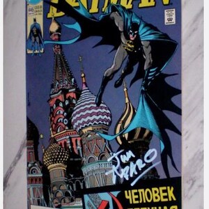 May include: Batman comic book cover featuring Batman in a dynamic pose against a backdrop of colorful onion-domed buildings. The cover includes the title "Batman" in large yellow letters and Russian text. Signed by Jim Aparo.