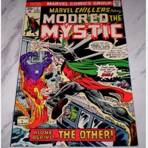 Puede incluir: Una portada de cómic vintage de Marvel Chillers con Modred the Mystic. La portada muestra una figura con capa roja y verde luchando contra un monstruo púrpura en medio de llamas. El texto incluye "Marvel Comics Group" y "Alone Against The Other!"
