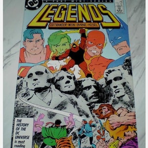 Puede incluir: Un cómic vintage titulado "LEGENDS" con varios superhéroes de DC Comics. La portada incluye a Superman, Batman y otros personajes, con el texto "THE HISTORY OF THE DC UNIVERSE is must reading."