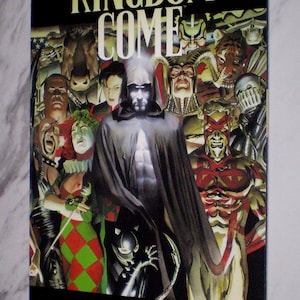 May include: A comic book cover for "Kingdom Come" featuring a group of costumed characters. The title is in large, yellow letters. The cover art includes a central figure in a dark cloak and a variety of other characters with unique designs. The authors' names are at the bottom.