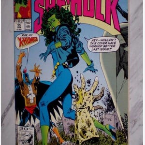 May include: A comic book cover featuring She-Hulk in a blue jumpsuit and jacket, with green skin and hair. The title "The Sensational She-Hulk" is in pink and white. Other characters are also depicted. The comic book is labeled "Marvel" and "35".