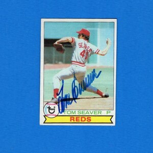 May include: A baseball card depicting Tom Seaver of the Reds in a pitching stance. He's wearing a red cap and uniform, with the number 41 visible. The card includes his signature and the Reds logo.
