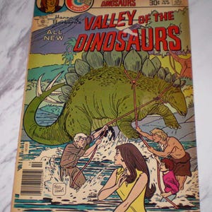May include: A vintage comic book titled "Valley of the Dinosaurs" by Hanna-Barbera. The cover features a green Stegosaurus being roped by people in a water scene. The comic book is from Charlton Comics.