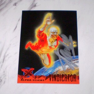 May include: A trading card depicting a superhero in a red and orange suit, with a white emblem, against a black backdrop. The card has the text "ALPHA FLIGHT" and "VINDICATOR" in red. The card is signed in silver ink.