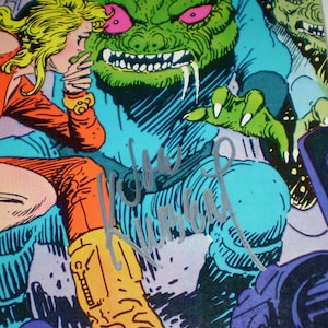 May include: Comic book illustration featuring a green monster with pink eyes and sharp teeth. A blonde woman in an orange outfit looks on in shock. The artwork is signed in silver ink.