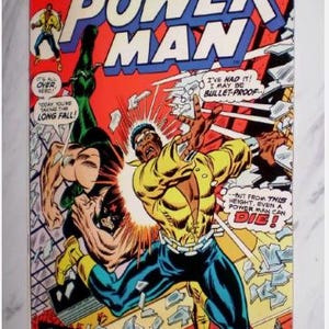 May include: Vintage comic book cover for Luke Cage, Power Man. The cover features a dynamic action scene with two figures in combat, set against a backdrop of shattered glass and city elements. The title and character names are prominently displayed.