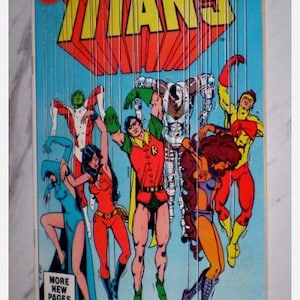 May include: Comic book cover for "The New Teen Titans" No. 9, featuring a group of costumed superheroes. The cover has a blue background with the title in yellow and red. The comic book is from July.