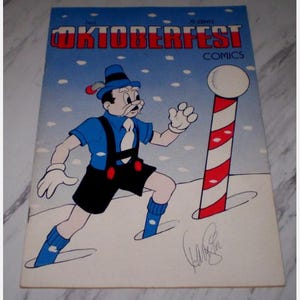 Peut inclure: Couverture de la bande dessinée "Oktoberfest Comics". L'illustration présente un personnage de dessin animé en costume bavarois, marchant dans la neige. Le fond est bleu avec des flocons de neige blancs. Un poteau rayé rouge et blanc est visible. Le titre est en rouge.