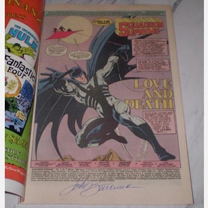 May include: Comic book page featuring a superhero in a dynamic pose with large wings. The title "Squadron Supreme" is visible, along with the words "Love and Death." The page includes text and a signature, with a partial view of another comic book on the left.