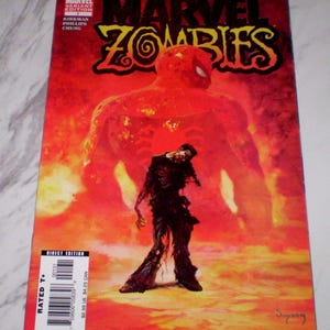 May include: A comic book cover for Marvel Zombies. The cover is predominantly red with the title "MARVEL ZOMBIES" in yellow. It features a large, fiery figure in the background and a zombie in the foreground. The cover includes the text "VARIANT EDITION" and "DIRECT EDITION".