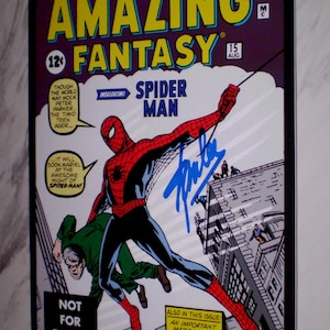 Puede incluir: Una portada enmarcada del c&oacute;mic Amazing Fantasy #15 con Spider-Man. La portada muestra a Spider-Man con un traje rojo y azul, balance&aacute;ndose por una ciudad, con el texto "Amazing Fantasy" y "Spider-Man". El c&oacute;mic est&aacute; firmado.