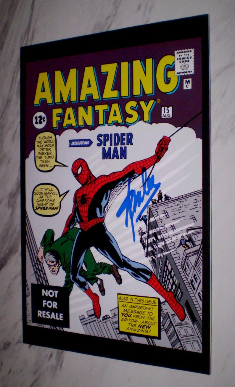 Puede incluir: Una portada enmarcada del c&oacute;mic Amazing Fantasy #15 con Spider-Man. La portada muestra a Spider-Man con un traje rojo y azul, balance&aacute;ndose por una ciudad, con el texto "Amazing Fantasy" y "Spider-Man". El c&oacute;mic est&aacute; firmado.