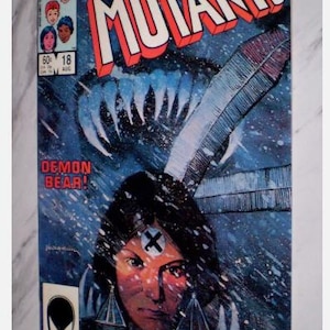 Puede incluir: Portada del cómic "The New Mutants" #18, con una mujer nativa americana con un símbolo de cruz en la frente. El título es en rojo y blanco, con un fondo azul y blanco. También se ven las palabras "Demon Bear!".