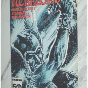 Puede incluir: Un cómic vintage titulado "The Warlord" de DC Comics. La portada presenta un guerrero con armadura y una espada, en tonos azules y negros. El título es rojo, con el texto "Morgan's Quest Continues Deathwatch!"