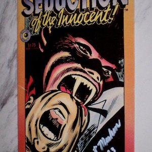 May include: Comic book cover titled "Seduction of the Innocent!" Part 3 of 3. The illustration depicts a vampire biting a person's neck. The comic is signed "Mort Meskin 1993."