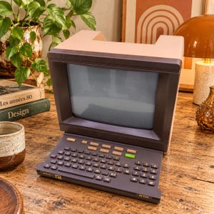 Könnte beinhalten: Ein Vintage-Minitel-1-Terminal mit einem dunkelgrauen Bildschirmgehäuse und einer passenden Tastatur im AZERTY-Layout. Das Gerät hat ein hellbeiges Obergehäuse, eine dunkelgraue Basis und enthält eine grüne Taste unter den Funktionstasten.