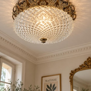 May include: A flush mount ceiling light fixture featuring a clear, diamond-patterned glass dome shade. The base is constructed from antique brass-toned metal with intricate, ornate scrollwork detailing and a small central decorative finial.