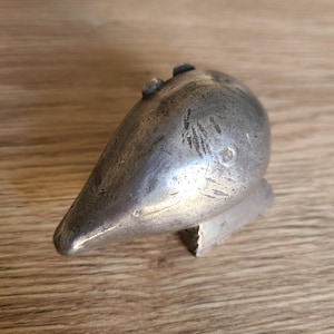 May include: A silver metal animal figurine shaped like a bird with a long beak. The figurine is sitting on a wooden surface.
