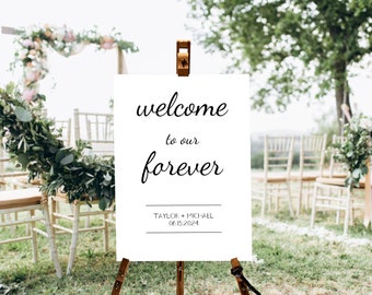 May include: A white sign on a wooden easel with the words "welcome to our forever" in elegant black script. Below, it reads "Taylor + Michael 06.15.2024". The sign is set up outdoors with chairs and floral arrangements, suggesting a wedding.