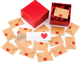 May include: A red gift box, open red box, and several small brown paper envelopes with red heart stickers. A white card with a red heart is also present. The items are arranged on a white surface, creating a romantic theme.