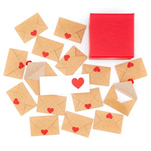 K&ouml;nnte beinhalten: Eine Anordnung kleiner, brauner Papierumschl&auml;ge mit roten Herzaufklebern, umgeben von einer roten Geschenkbox und einer wei&szlig;en Karte mit einem roten Herz. Einige Umschl&auml;ge sind versiegelt, einer ist ge&ouml;ffnet.