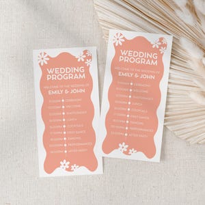 Puede incluir: Dos tarjetas de programa de boda con un diseño ondulado de color melocotón y texto blanco. El texto dice "PROGRAMA DE BODA" y enumera el programa de la boda. Acentos de margaritas blancas en la parte inferior. Los programas están sobre un fondo neutro.