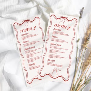 May include: Two white menu cards with red text and decorative borders, featuring a menu for a meal. The word "menu" is at the top. The cards are on a white, textured surface, with wheat and lavender sprigs.
