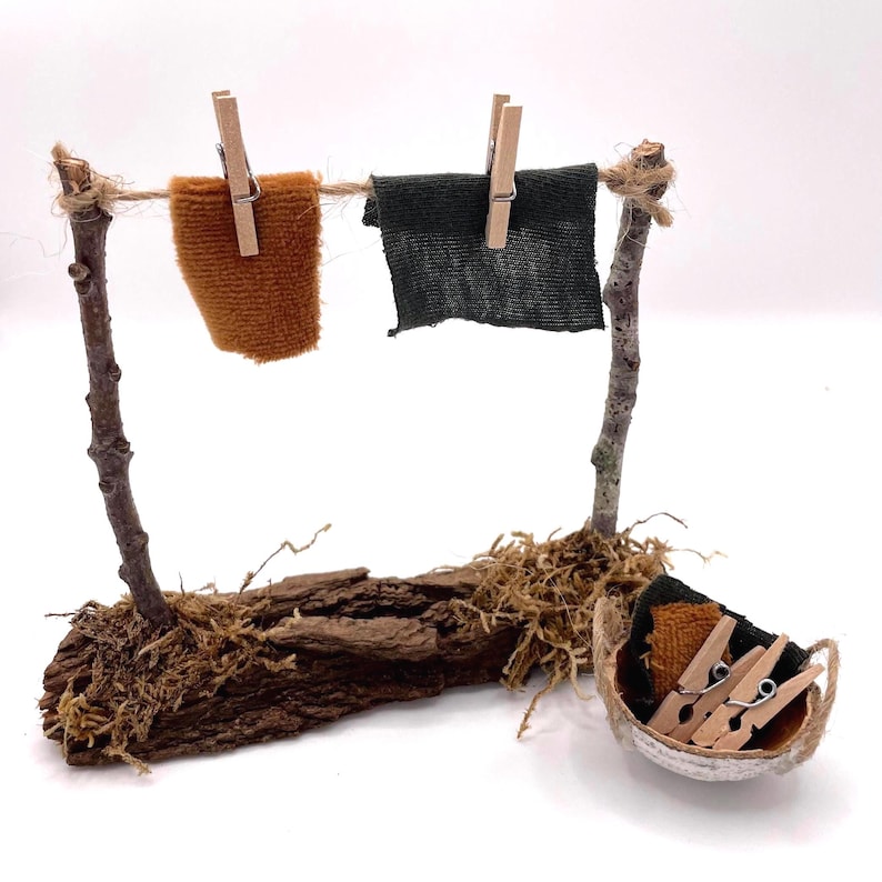 K&ouml;nnte beinhalten: Eine Miniatur-W&auml;scheleine aus Zweigen und Schnur, mit zwei kleinen Stoffquadraten, die mit Holzklammern an der Leine befestigt sind. Ein kleiner Korb enth&auml;lt zus&auml;tzliche W&auml;scheklammern und Stoffst&uuml;cke. Die Basis besteht aus Rinde und Moos.