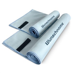 May include: Two light blue microfiber towels rolled up with black elastic bands. The towels are printed with the text "Wunschname" in dark blue.