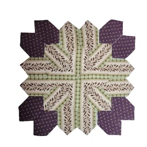 May include: A handcrafted quilt block featuring a starburst design. The block combines fabrics with floral and plaid patterns in shades of purple, green, and cream. The central design showcases a cream fabric with brown leaf patterns.