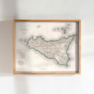 May include: Framed vintage map of Sicily, Italy, with detailed topography and coastlines highlighted in green. The map is encased in a light brown wooden frame, perfect for home decor. The map includes the text "Carta Moderna di Sicilia".