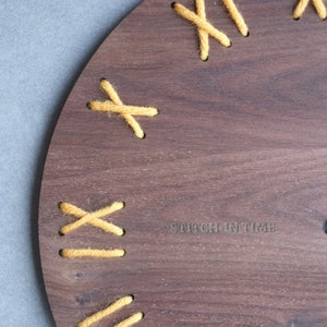 May include: A wooden clock face with yellow yarn stitched in an X pattern around the edge. The text "Stitch in Time" is printed on the face.