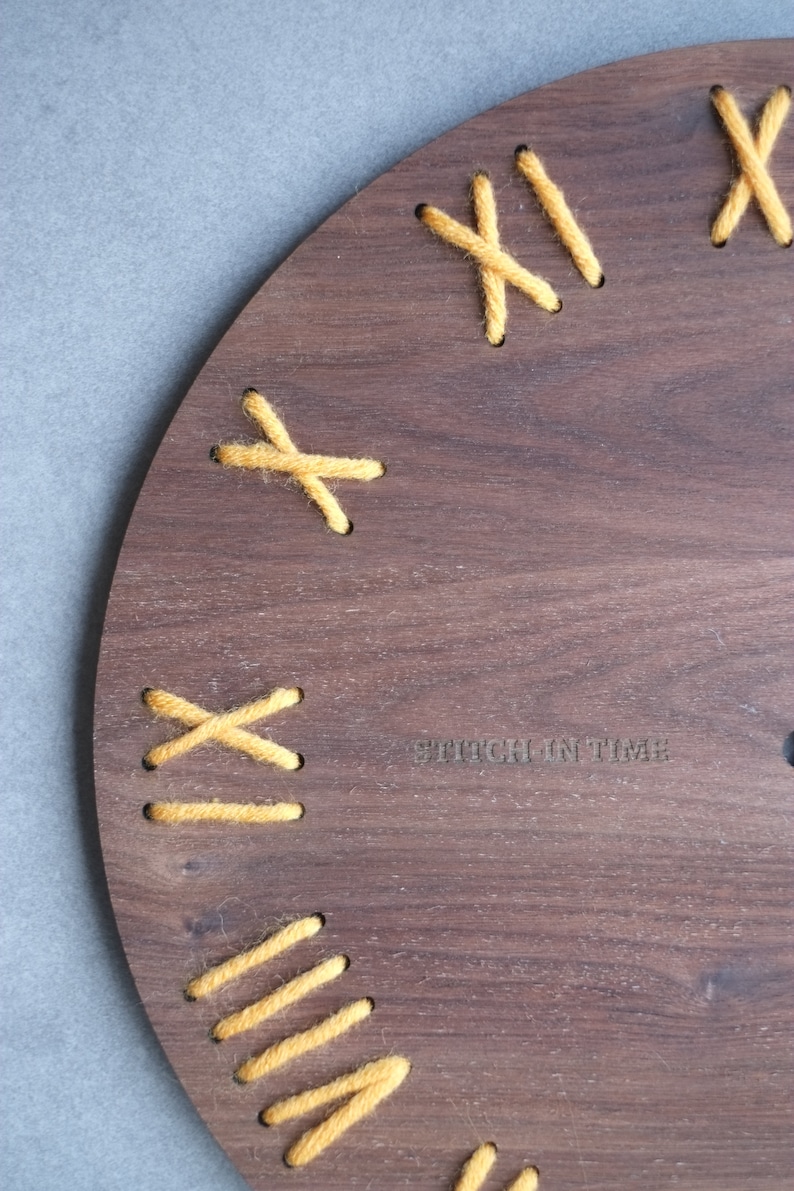 May include: A wooden clock face with yellow yarn stitched in an X pattern around the edge. The text "Stitch in Time" is printed on the face.