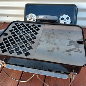 May include: Black Weber charcoal grill with a removable grate and a lid with a handle. The grill has a black metal frame and a silver metal grate. The lid has a black handle and a silver metal knob.