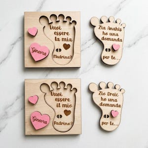 May include: Two square wooden plaques and two foot-shaped wooden cutouts featuring engraved Italian text. The plaques include pink heart-shaped wooden pieces with the name Ginevra. The text reads: Vuoi essere la mia Madrina, Vuoi essere il mio Padrino, Zia Anahis ho una domanda per te, and Zio Dreic ho una domanda per te.
