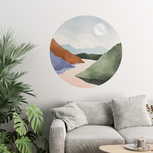 May include: A circular wall decal featuring a watercolour-style landscape design. The scene depicts a river flowing through a valley with mountains in the background. The colours are muted and include shades of blue, green, brown, and pink. A white moon is visible in the sky.
