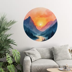 Könnte beinhalten: Ein runder Wandaufkleber mit einer Aquarellmalerei einer Bergkette mit einem See im Vordergrund. Der Himmel ist in leuchtenden Orange- und Rosatönen gehalten, mit einer strahlend gelben Sonne, die hinter den Bergen untergeht.