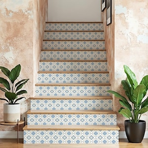 Op de afbeelding: Trap met stootborden versierd met blauwe en crèmekleurige bloempatroonstickers. De houten treden worden geflankeerd door potplanten en staan tegen een getextureerde, perzikkleurige muur.