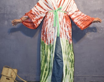 May include: A white, red, and green tie-dye kimono with a green sash. The kimono is worn over blue jeans and the person is wearing a white hat and gold sandals.