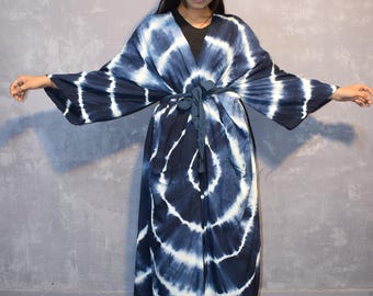 Puede incluir: Un kimono largo de color azul y blanco con estampado tie-dye, de silueta ancha y fluida. El kimono tiene cuello en V y mangas largas, y se ata a la cintura con una cinta a juego.