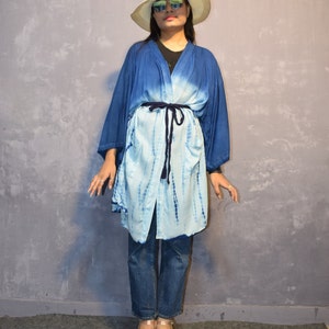 Könnte beinhalten: Ein blaues und weißes Batik-Kimono mit einem schwarzen Gürtel. Das Kimono wird über Jeans und einem schwarzen Shirt getragen. Die Person trägt einen weißen Hut und eine Sonnenbrille.