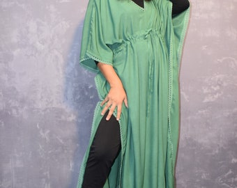 May include: A green maxi dress with a long, flowing silhouette and a drawstring waist. The dress has a V-neckline and lace trim around the edges. The model is wearing the dress with black leggings and sandals.