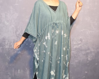 May include: A long, flowing, teal blue kaftan with a white tie-dye pattern. The kaftan has a V-neck and a drawstring waist. The sleeves are three-quarter length and have a lace trim. The kaftan is worn with black pants and black sandals.