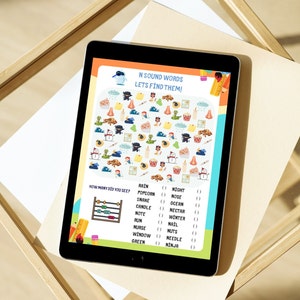 Puede incluir: Una tableta que muestra una hoja de actividades educativa sobre palabras con el sonido N. La p&aacute;gina presenta un juego de buscar y encontrar con ilustraciones de serpientes, narices y ninjas, junto a una lista de palabras para contar.